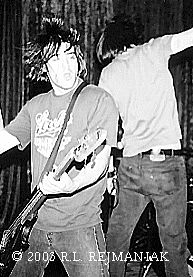 Black-and-white performance photograph of a musician playing bass or guitar.